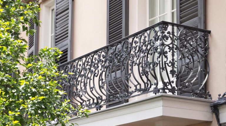 Close-up of a historic wrought-iron balcony with intricate patterns against a neutral-toned building exterior, captured at midday with soft, blurred background.